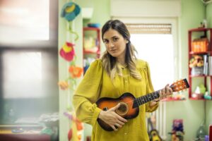 Une femme tient une petite guitare pour enfant dans une pièce verte.