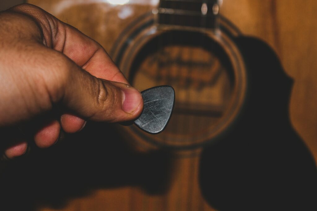 Une main tient un plectre devant la rosace de son instrument à cordes.