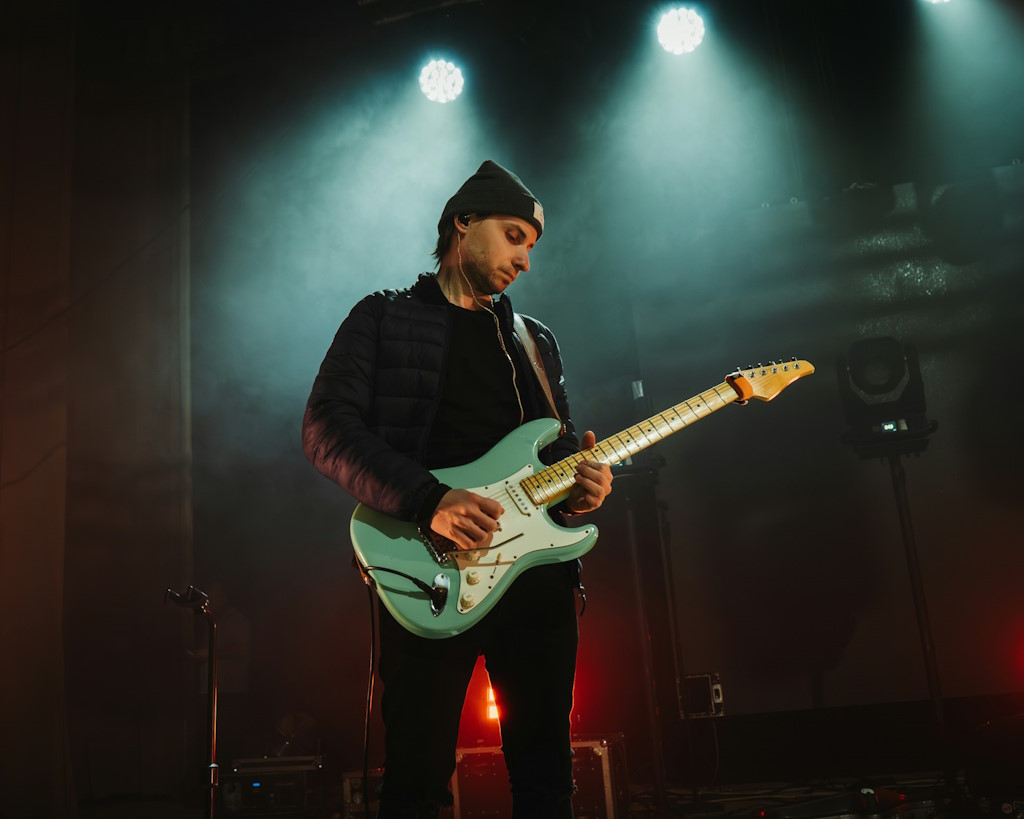 Un guitariste se tient sur scène, sous les lumières lors d'un live.