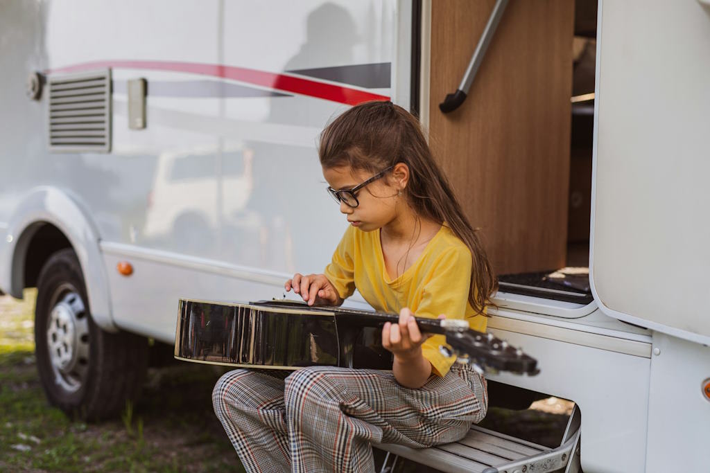 Une petite fille joue de la musique sur les marches d'un camping-car.