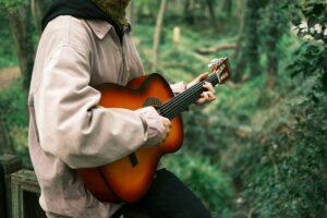 Une guitariste joue de la guitare en pleine nature, dans une forêt.
