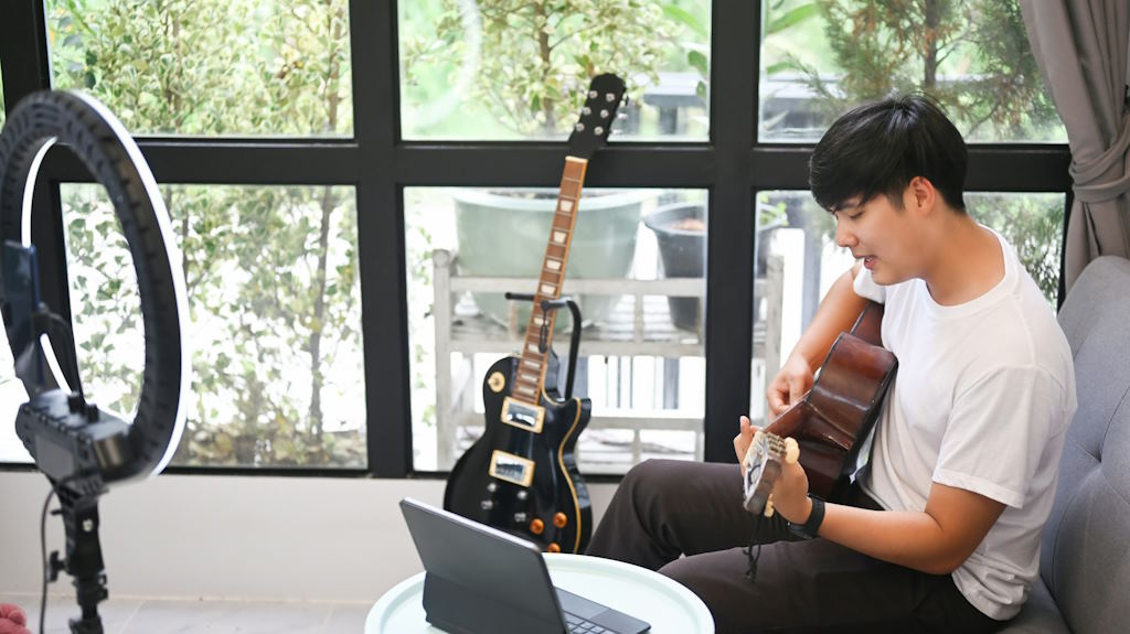 Un guitariste s'entraîne sur une guitare, assis sur un canapé.