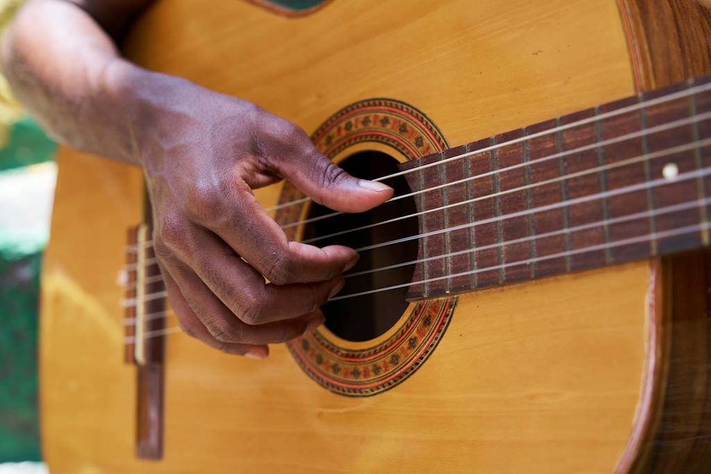Gros plan sur la rosace d'une guitare acoustique et sur une main grattant les cordes.