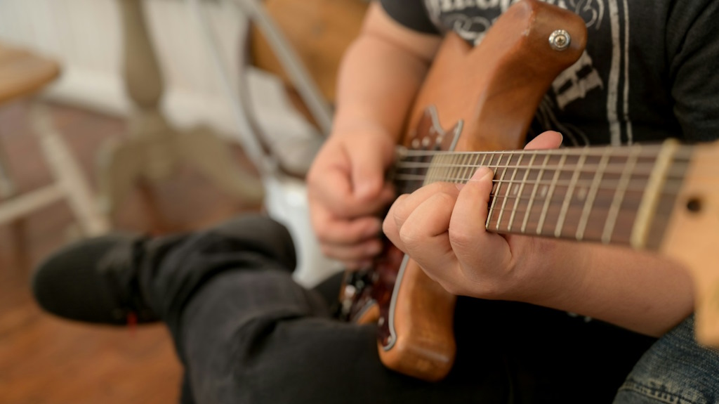 Un guitariste joue dans un salon, la jambe gauche posée sur la jambe droite.
