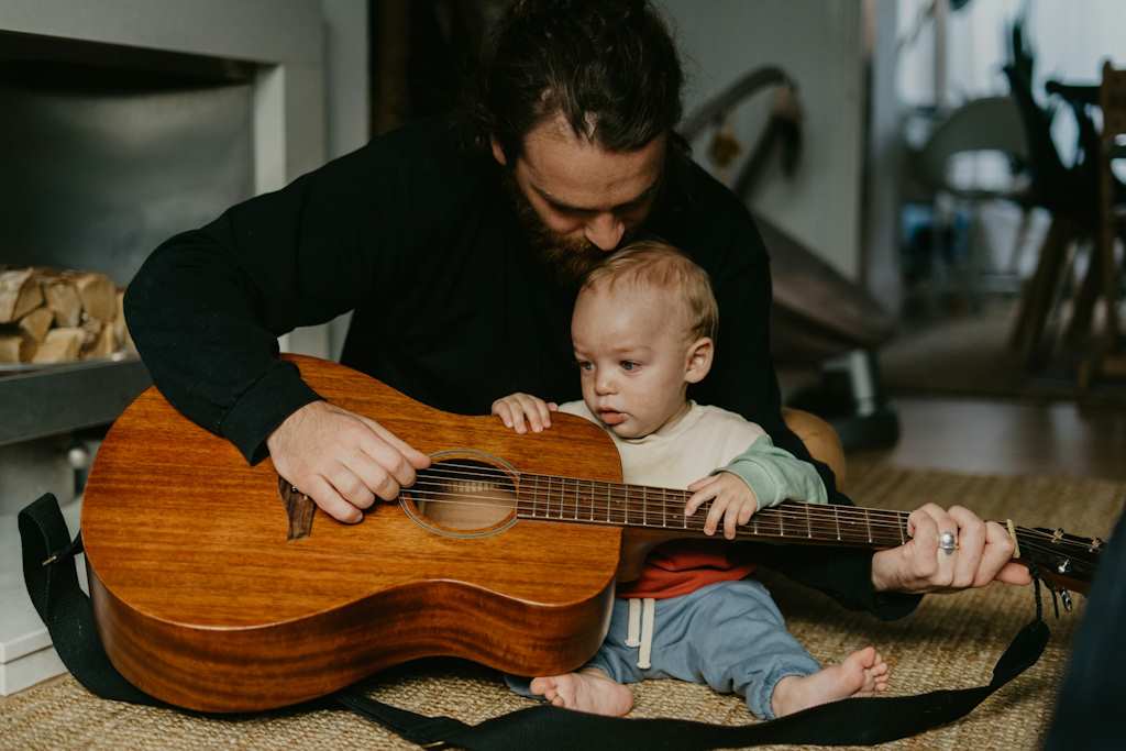 Un père de famille semble initier son enfant à la guitare.