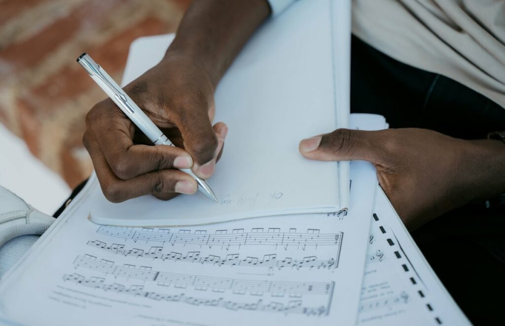 Un homme en train d'écrire un titre sur une feuille blanche par dessus une partition musicale.