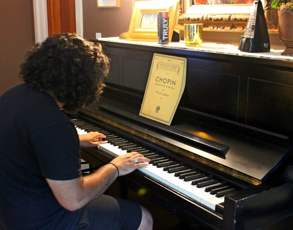 Un pianiste vue de derrière, sur son côté droit, en train de jouer au piano devant un livre de partitions de F. Chopin.