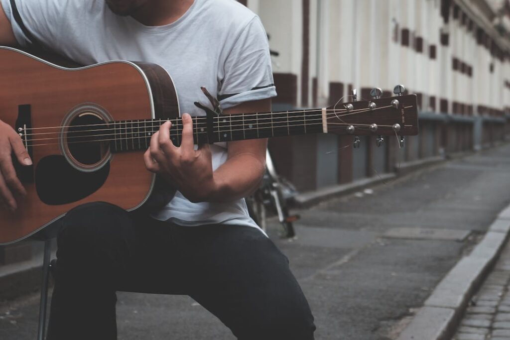 Un guitariste joue dans une rue assez terne, au pied de bâtiments blancs.