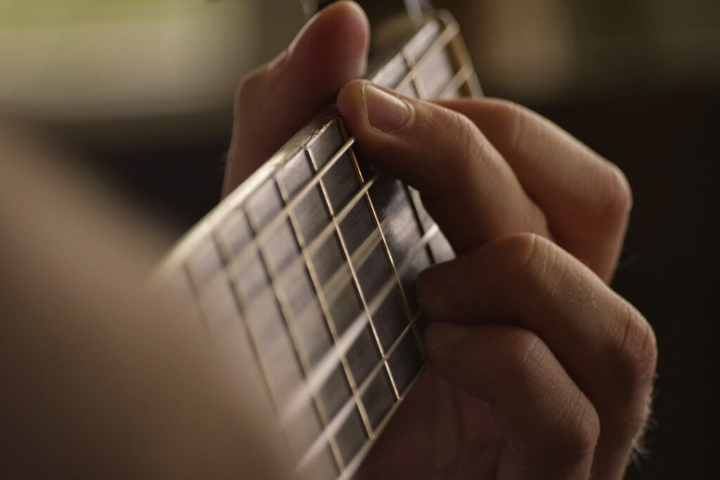 Vue en gros plan sur les doigts d'un guitariste jouant un accord enrichi à quatre notes.