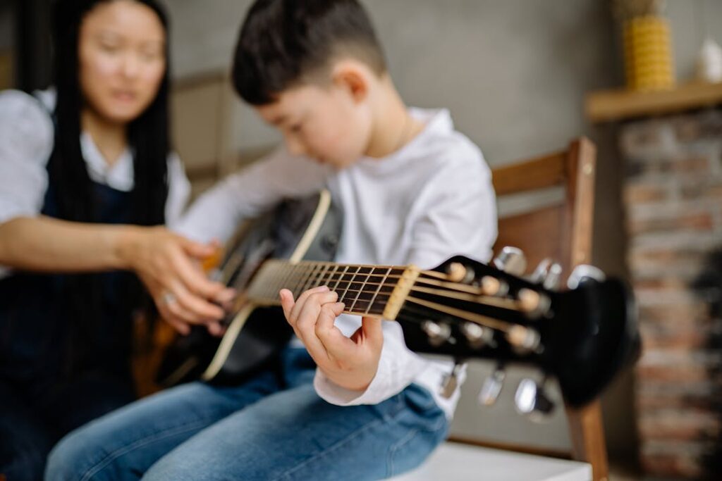 Une dame donne un cours de guitare à un petit enfant.