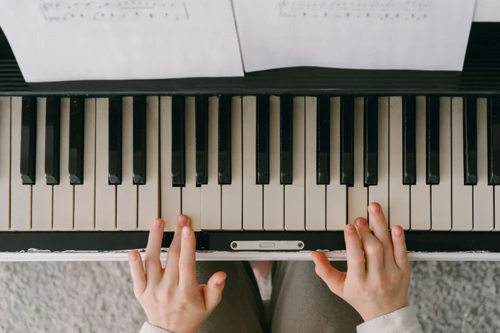 Deux mains d'une personne qui joue du piano avec une partition sur le pupitre.