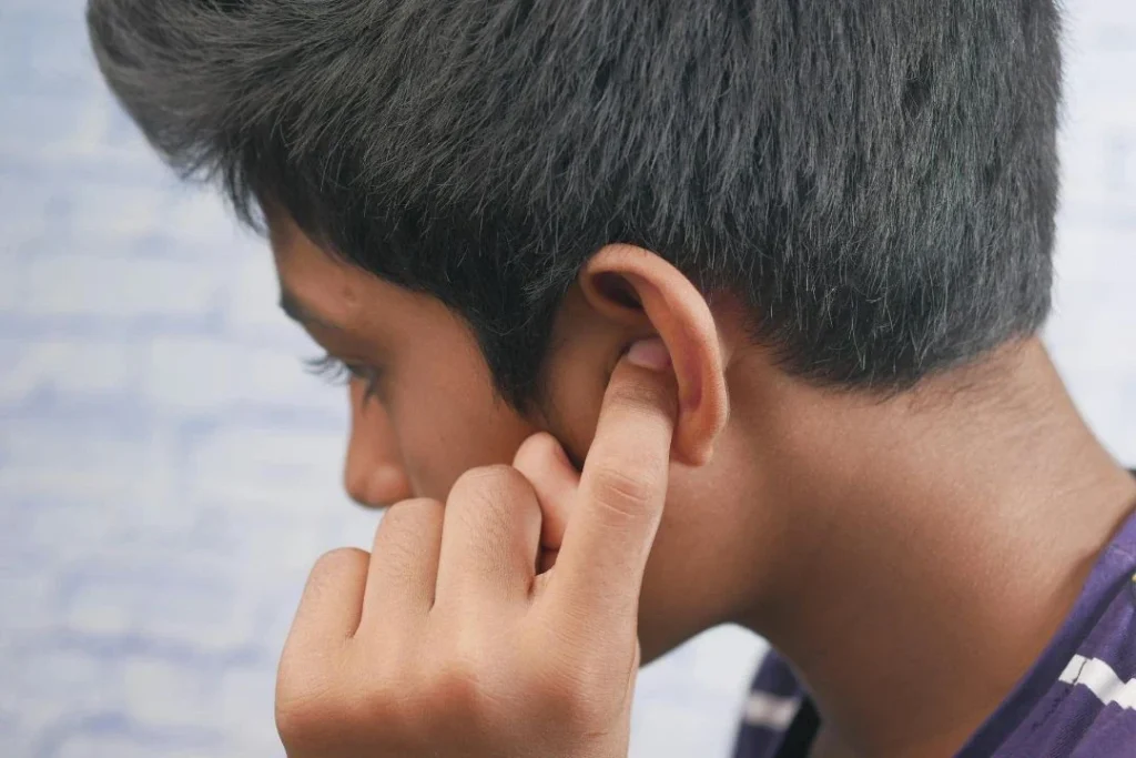 Un jeune garçon vu de profil, se tient l'oreille gauche.