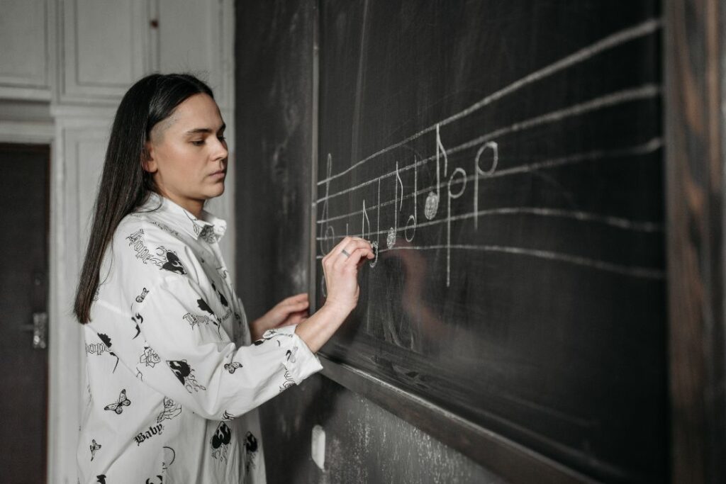 Une étudiante est debout dans une classe pour colorier des notes sur une portée dessinée au tableau.