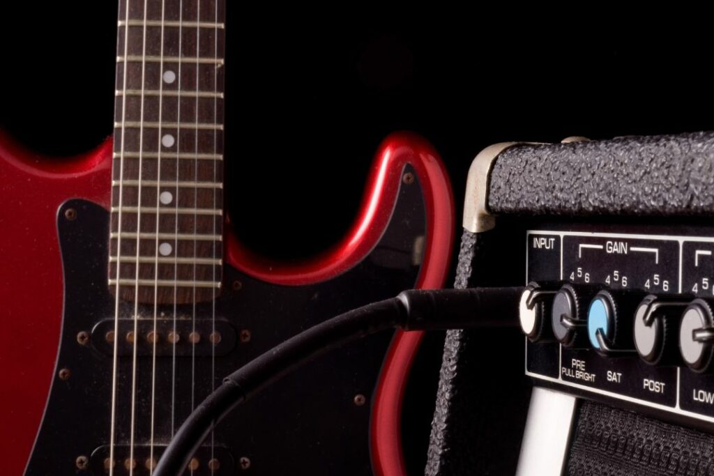 Une guitare électrique rouge et noire avec un jack branché sur l'amplificateur.