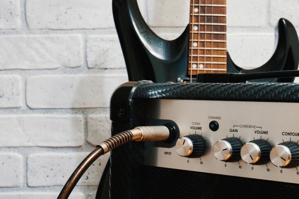 Un ampli, un jack et une guitare noire posée contre un mur blanc.
