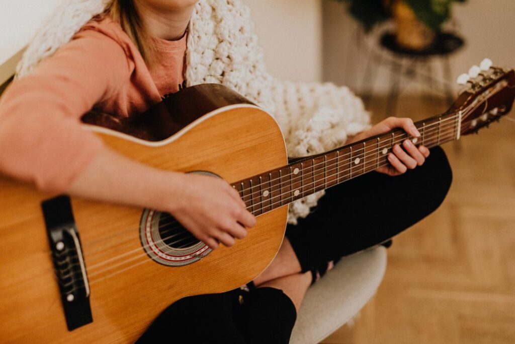 Une femme qui joue de la guitare sur son sol chez elle.
