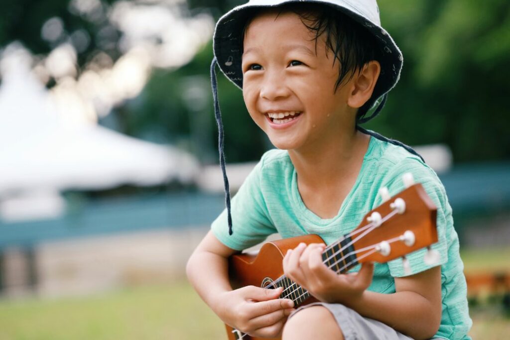 Enfant souriant jouant du ukulélé soprano en extérieur.