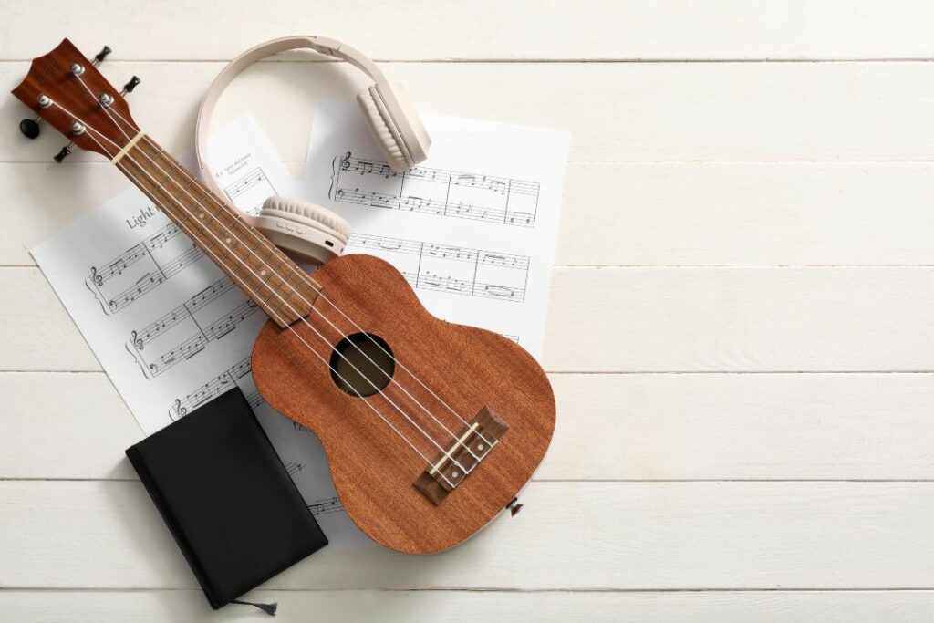 Ukulélé en bois posé sur des partitions avec un casque audio et un carnet.
